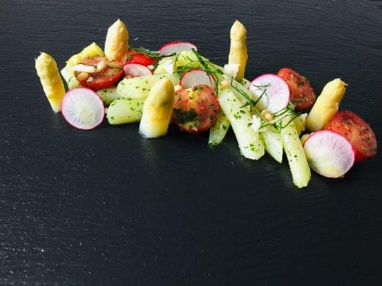 Gourmetsalat mit weißem Spargel, Radieschen, Tomaten, Kräutern und Pinienkernen auf schwarzem Schiefer